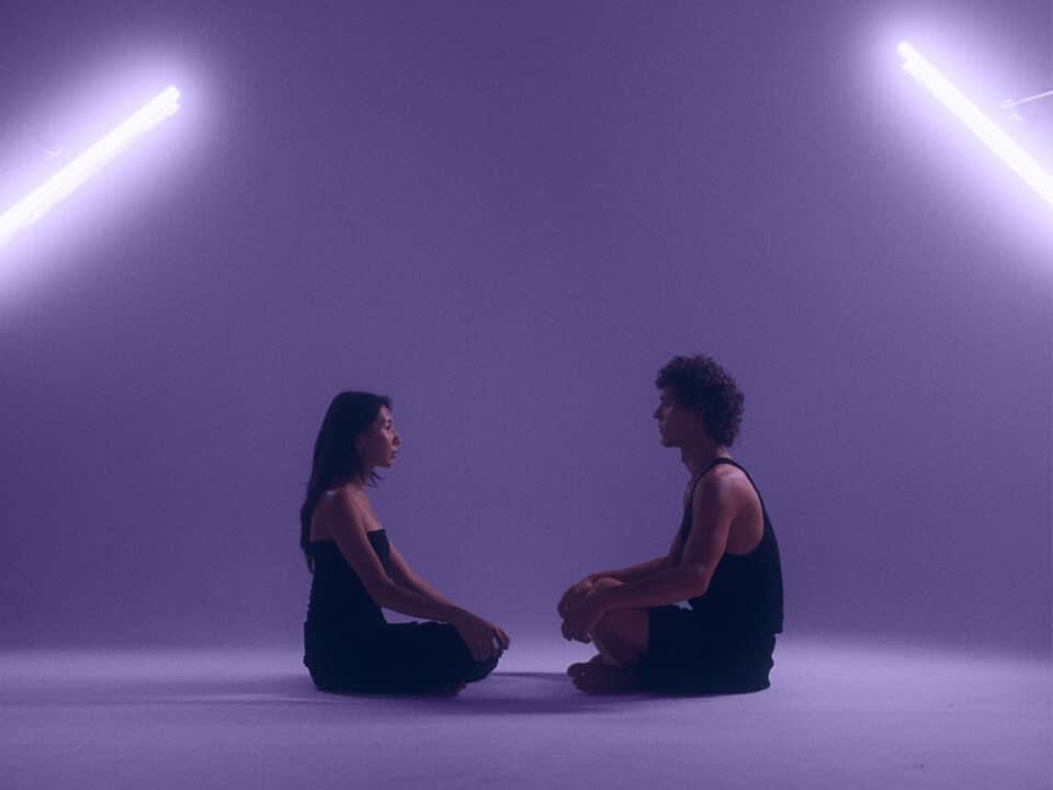 Woman sitting cross legged in front of man sitting crosslegged with dark purple background